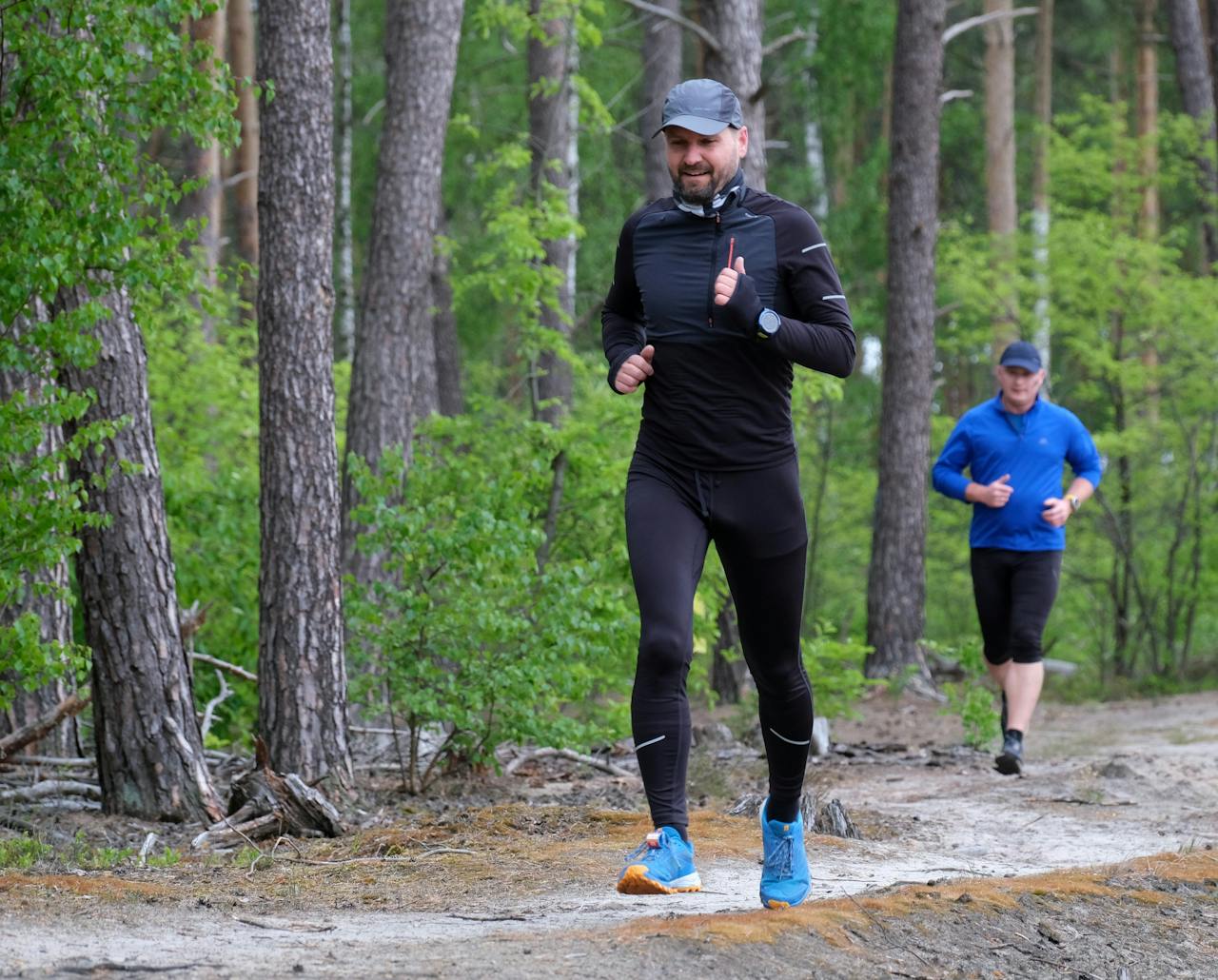 services-01 Outdoor exercise scene with two men jogging through a lush green forest trail, wearing sports attire.