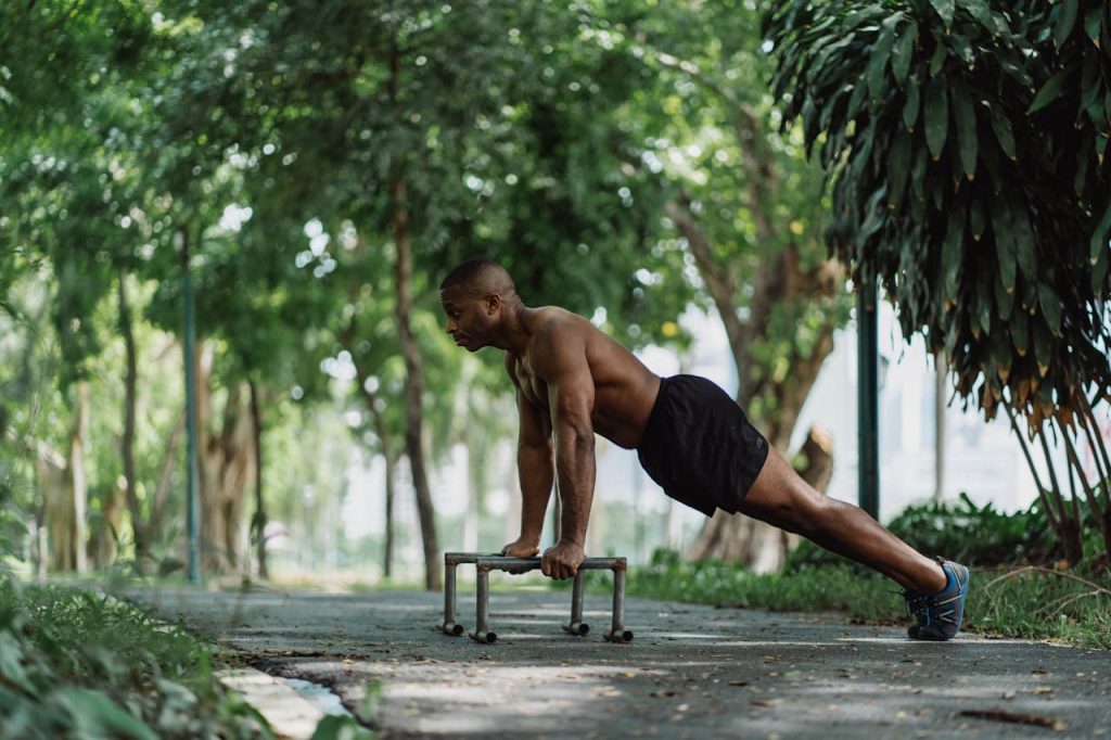 pexels photo 4804025 Athletic man doing push-ups on low bars in a lush green park, focusing on fitness and nature.