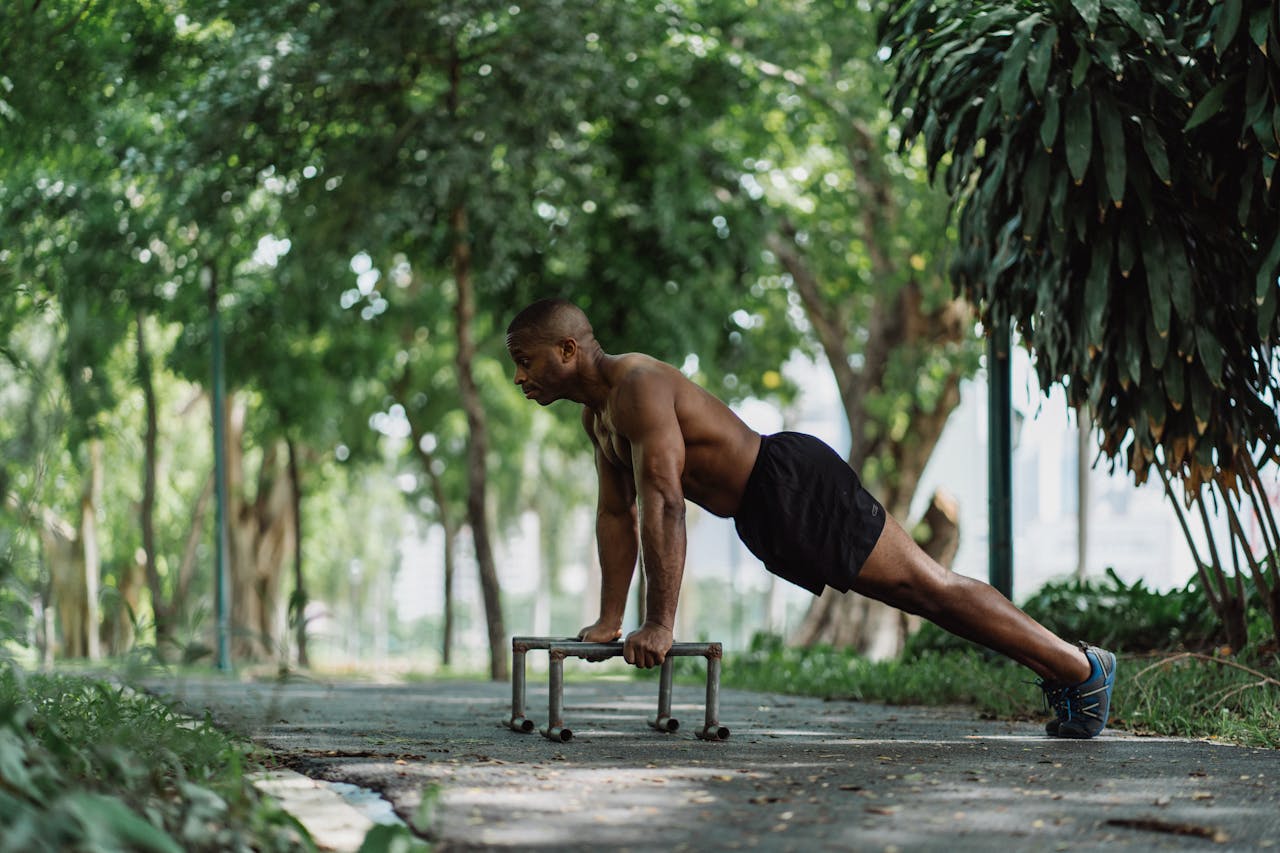 services-03 Athletic man doing push-ups on low bars in a lush green park, focusing on fitness and nature.