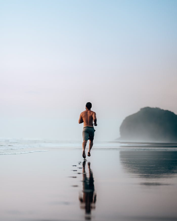 services-02 Back view full length shirtless sporty male jogging on picturesque wet sandy beach on foggy morning
